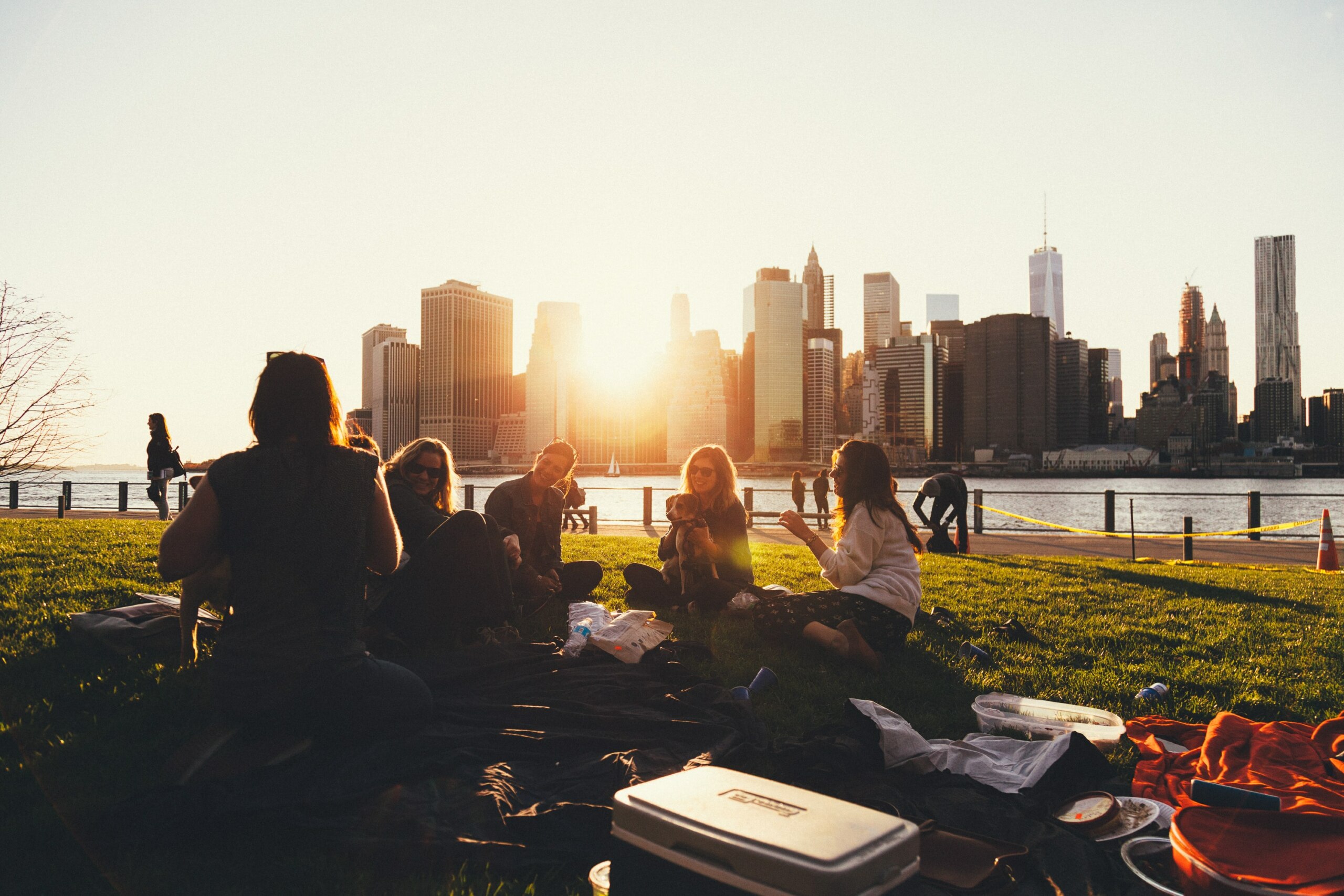 group of people sit outside together with a sunset and city skyline in the background.