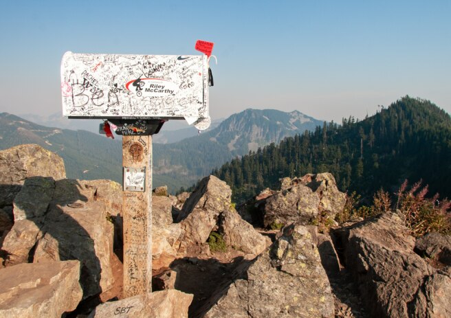 Mailbox on a wooden post overlooking a mountain range.