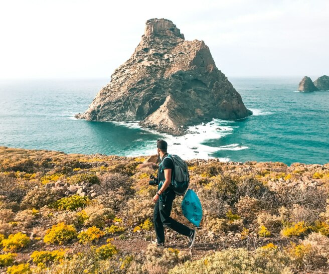 Man carrying a trash bag on a trail overlooking the ocean.